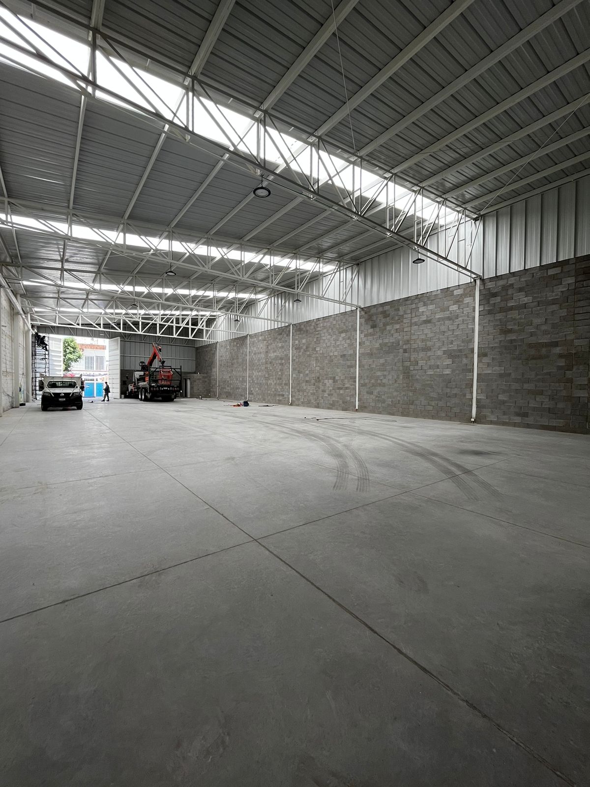 Interior amplio de bodega Valtierra con sistema de iluminación industrial y piso terminado, Fer Et Ciment León